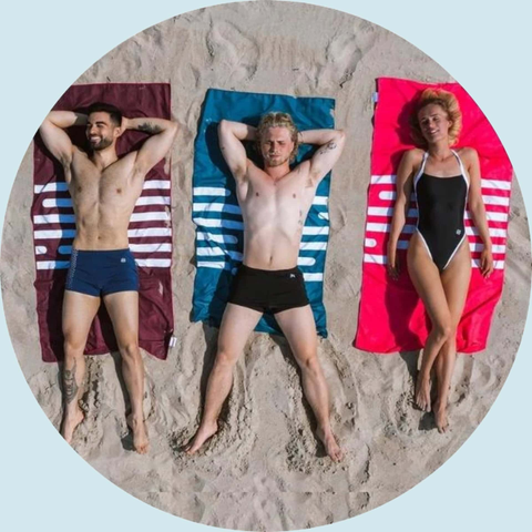 2 mænd og 1 kvinde ligger på håndklæder på stranden.